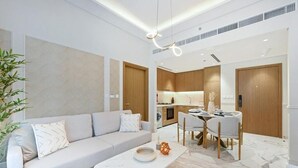 A modern living room with a sofa, a dining table, and a kitchen in the background. - 221Bloomfields Grandr2BRAzizi Riviera 67 (Dubai)