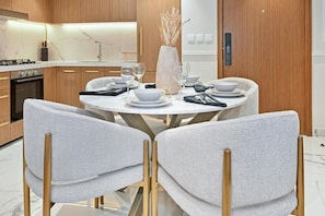 A modern kitchen with a round dining table, white chairs, and a vase with dried plants. - 221Bloomfields Grandr2BRAzizi Riviera 67 (Dubai)