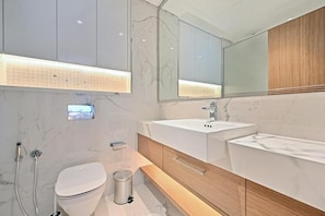 A modern bathroom with a white toilet, a large mirror, a white sink, and a shower area. - 221Bloomfields Grandr2BRAzizi Riviera 67 (Dubai)