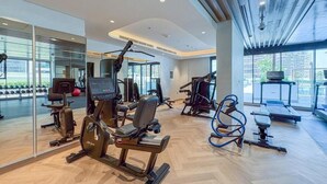 A modern gym with cardio machines, weight training equipment, and a mirrored wall. - 221Bloomfields Grandr2BRAzizi Riviera 67 (Dubai)