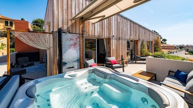 Ein moderner Außenbereich mit Whirlpool, Holzterrasse, Liegestühlen und einer Pergola.