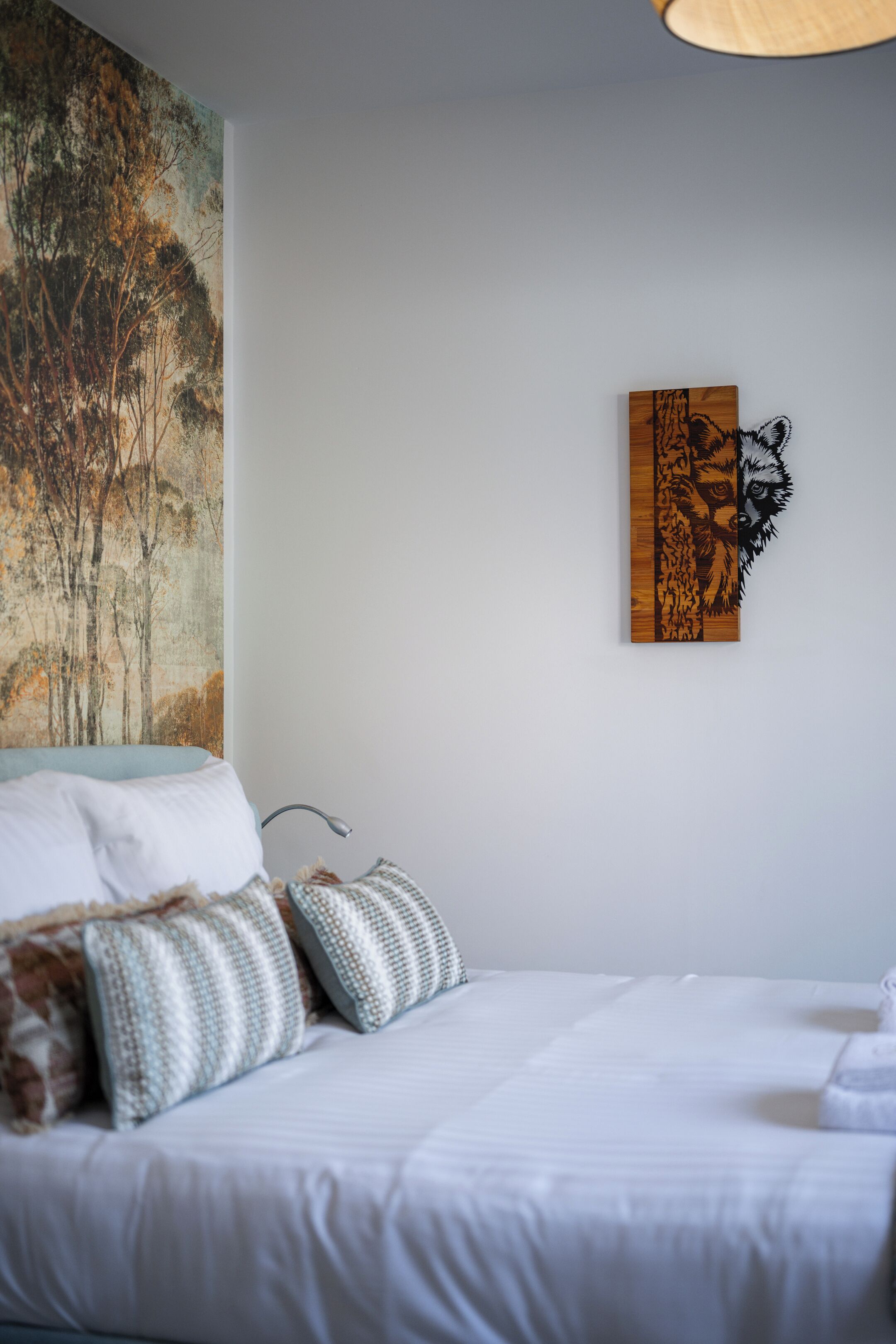 A bedroom with a bed, pillows, a wall painting, and a wooden artwork.