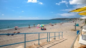 Ein Strand mit Sonnenschirmen, Menschen und blauem Himmel.