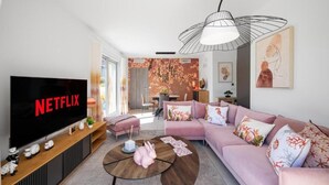 Ein modernes Wohnzimmer mit Flachbildfernseher, einem rosafarbenen Sofa, einem Couchtisch und einem Essbereich im Hintergrund.
