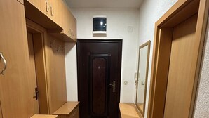 Un couloir étroit, avec des armoires en bois et une porte sombre au fond.