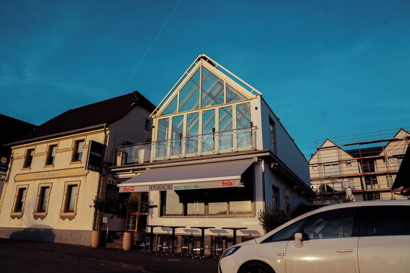 A building with a glass front, outdoor seating, and a Coca-Cola sign. - Hotel am Hafen Leverkusen (Leverkusen)
