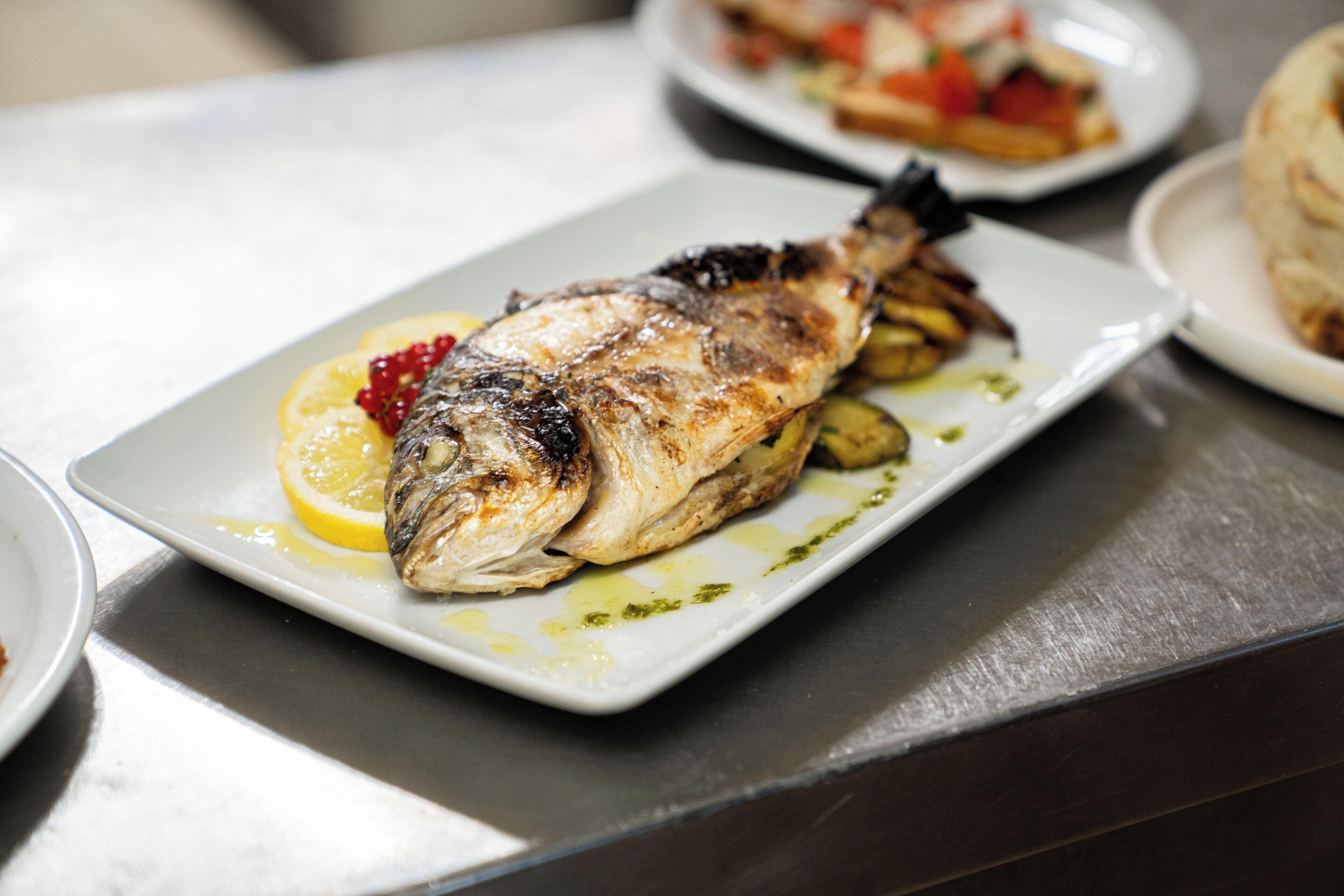 Un plato con un pescado a la parrilla, una rodaja de limón y algunas verduras.