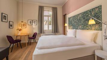 A hotel room with a large bed, a small table with chairs, a desk, and a window with curtains.