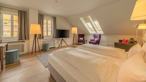 A spacious bedroom with a large bed, two standing lamps, a flat-screen TV, and a skylight.