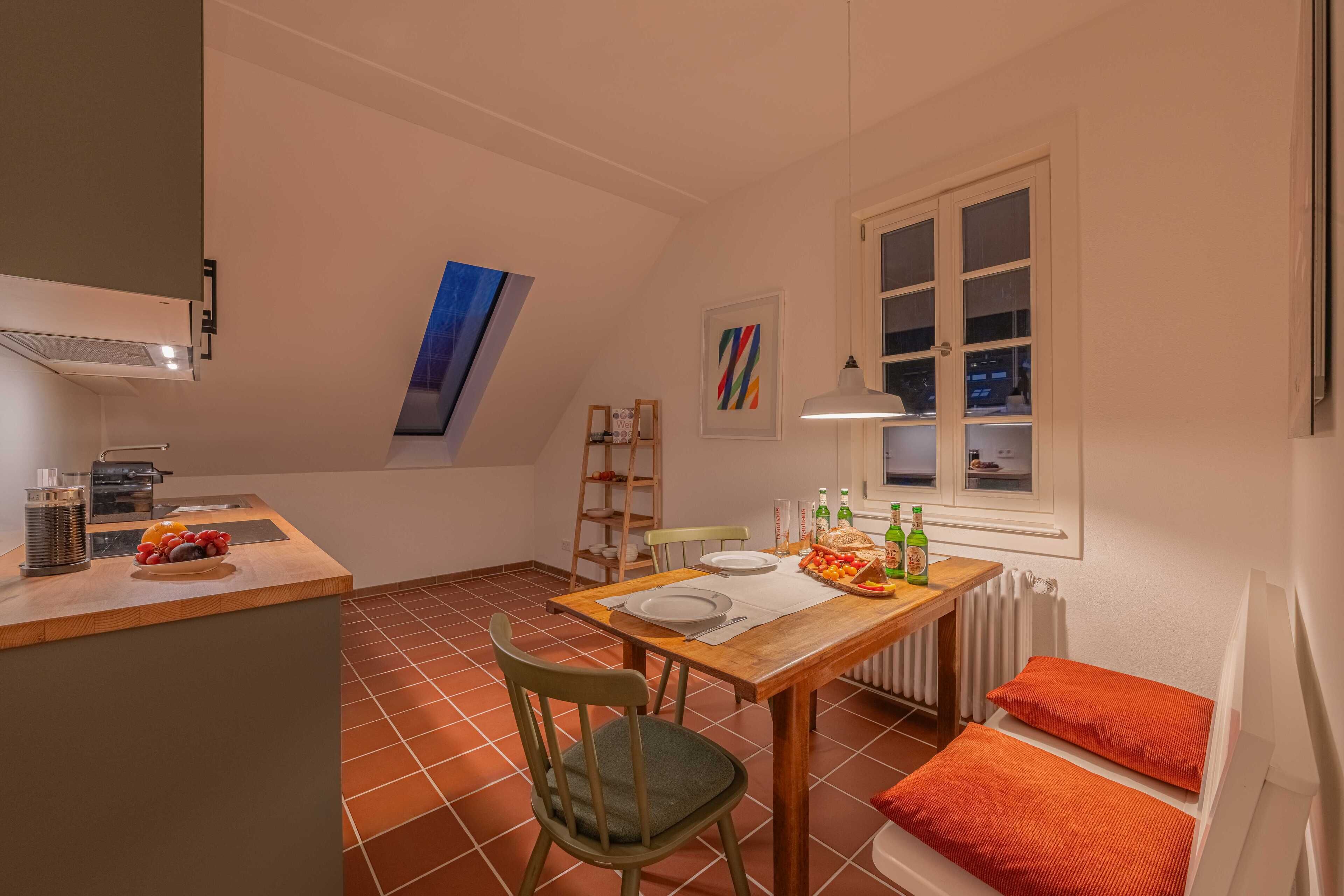 A compact kitchen with a dining area, a window with blinds, and a radiator.