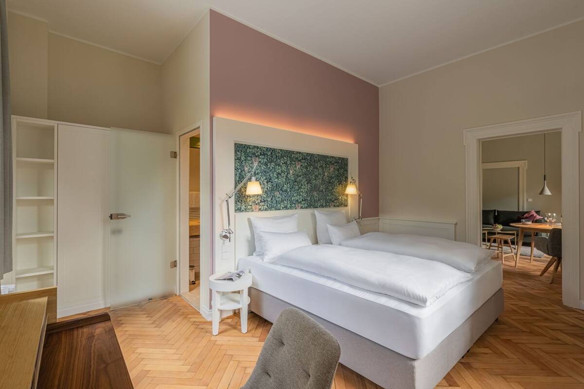A bedroom with a large bed, a bedside table, a chair, a wardrobe, and a desk.