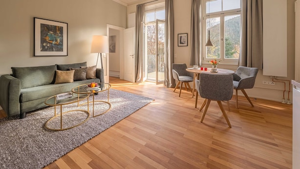 A modern living room with a green sofa, a round coffee table, and a dining area with a small table and chairs.