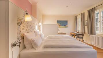 A hotel room with a large bed, a desk, and a chair. There is a window with curtains and a painting on the wall.
