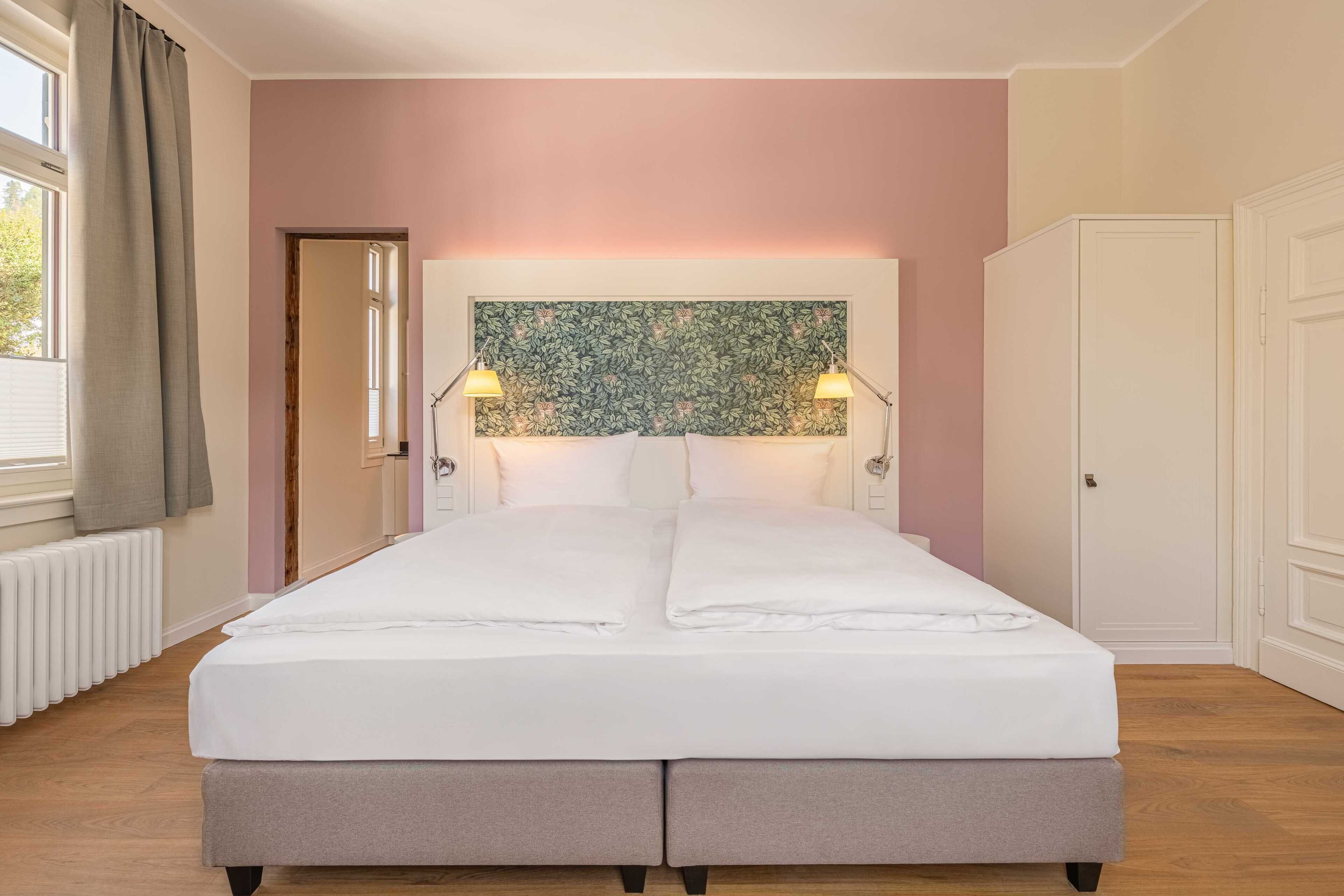 A double bed with white linens, two bedside lamps, a floral headboard, and a radiator on the left.