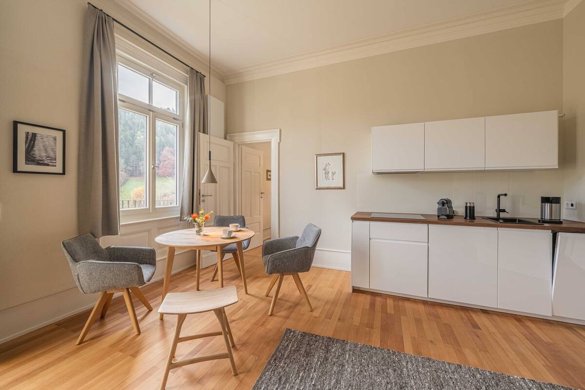 A modern kitchen with white cabinets, a wooden countertop, and a dining area with two chairs and a table.