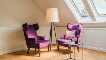 A room with two purple velvet armchairs, a floor lamp, and a small table with a wine bottle and glass.