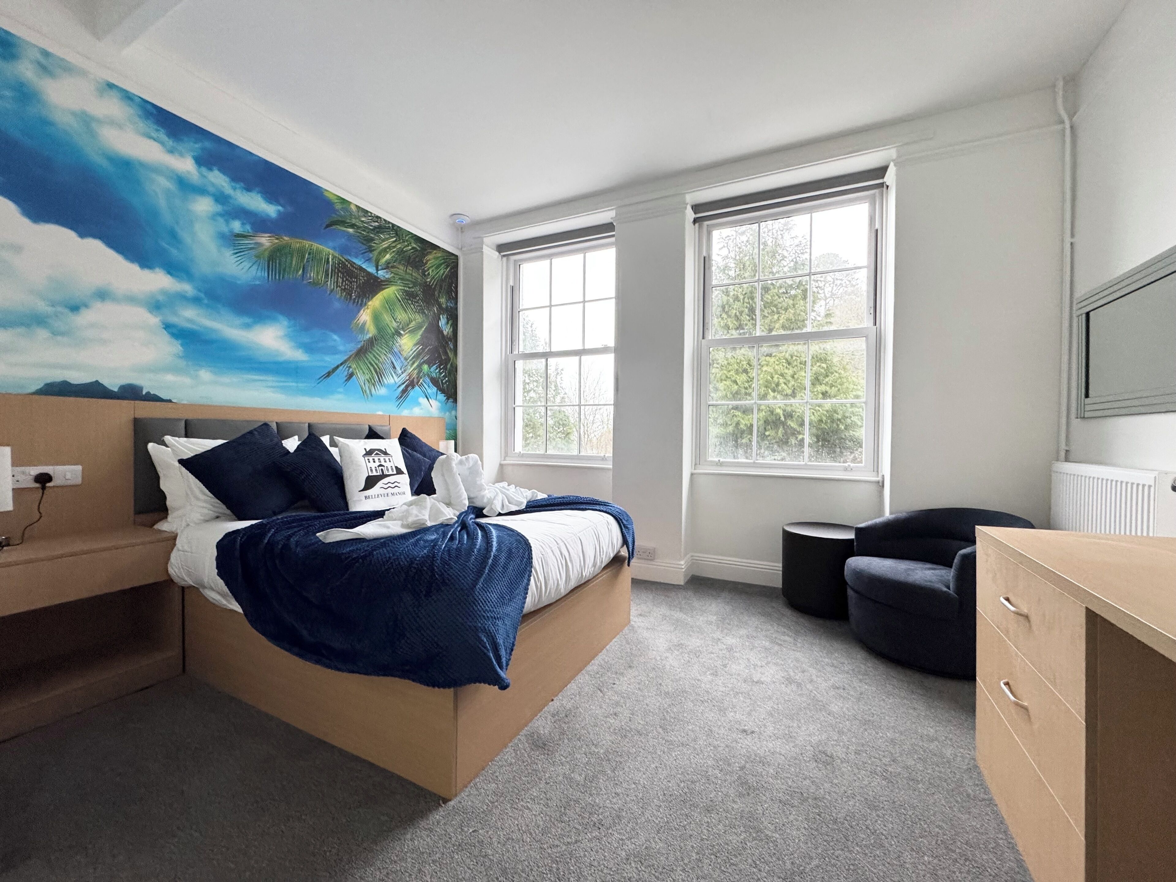 Une chambre à coucher comprenant un lit, une table de chevet, une commode, une chaise et une grande fenêtre.