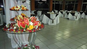 Une salle de banquet où les tables sont recouvertes de nappes blanches et où une composition centrale de fruits et de fleurs attire l’attention.