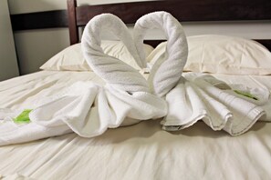 Un lit avec du linge de lit blanc et deux serviettes disposées en forme de cœur.