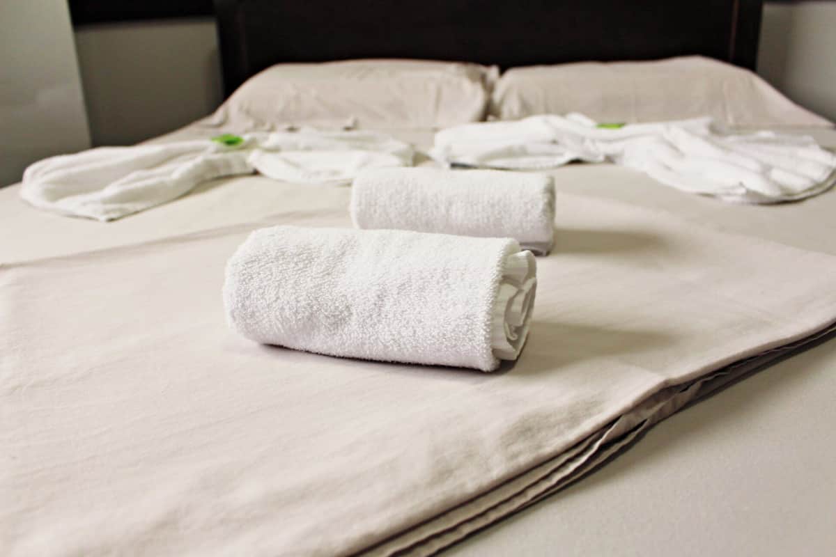 Un lit bien fait, avec des draps blancs et une serviette enroulée posée sur le dessus.