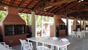 Une terrasse extérieure avec des fours en briques, des chaises et des tables en plastique blanc.