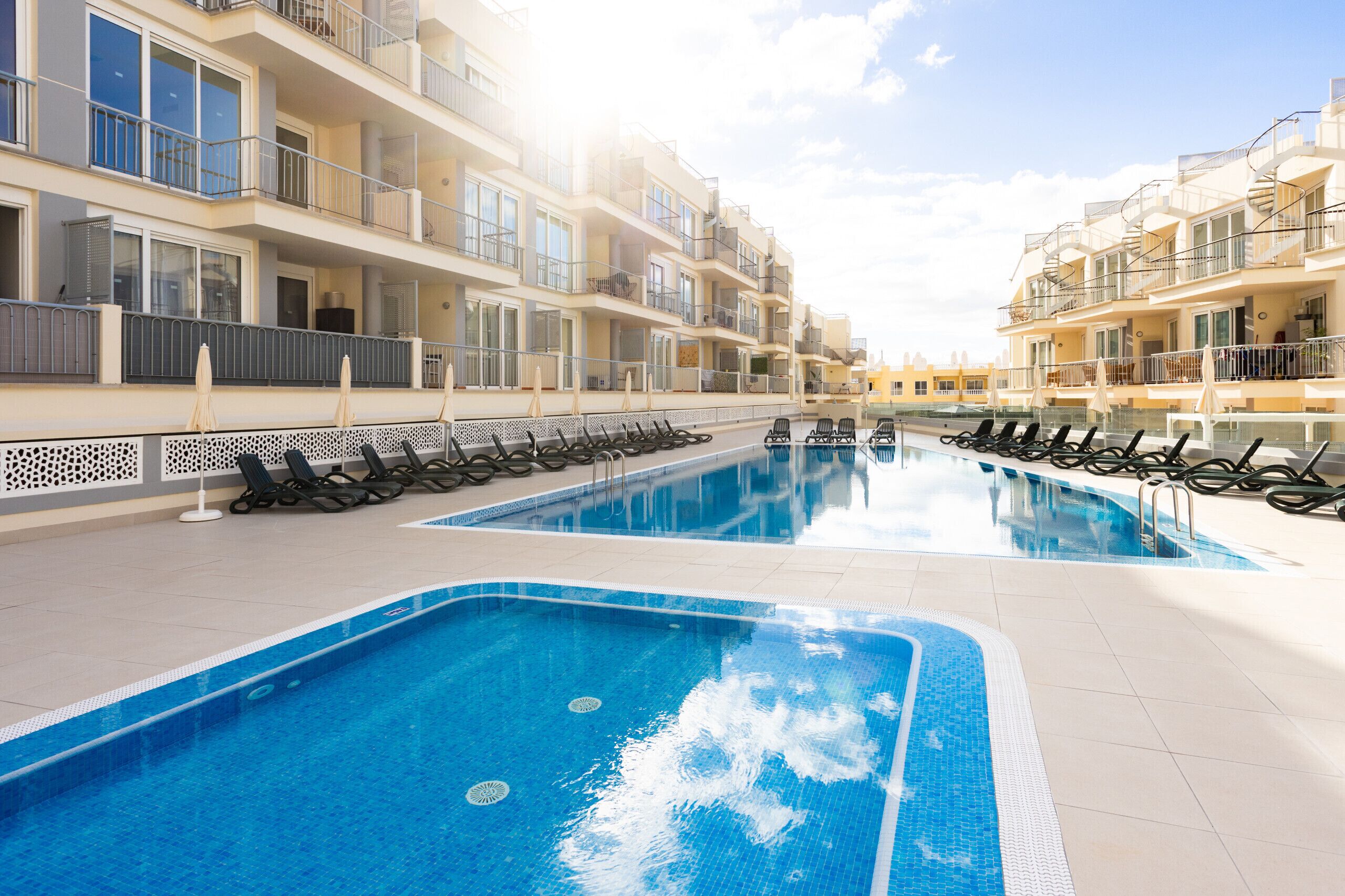 Une piscine avec des chaises longues et un bâtiment doté de balcons.