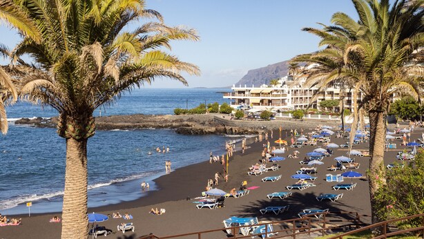 Een strand met palmbomen, parasols en ligbedden.