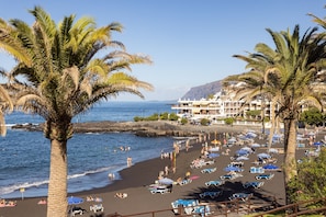 A beach with palm trees, umbrellas, and lounge chairs. - Relaxation, Sun, Pool, and Ocean in Puerto de Santiago   (Puerto de Santiago)
