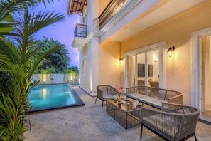 A poolside area with a dining set and chairs, a small table with a vase of flowers, and a view of the pool. - Elivaas Casa Zyra 4 BHK villa (Mapusa)