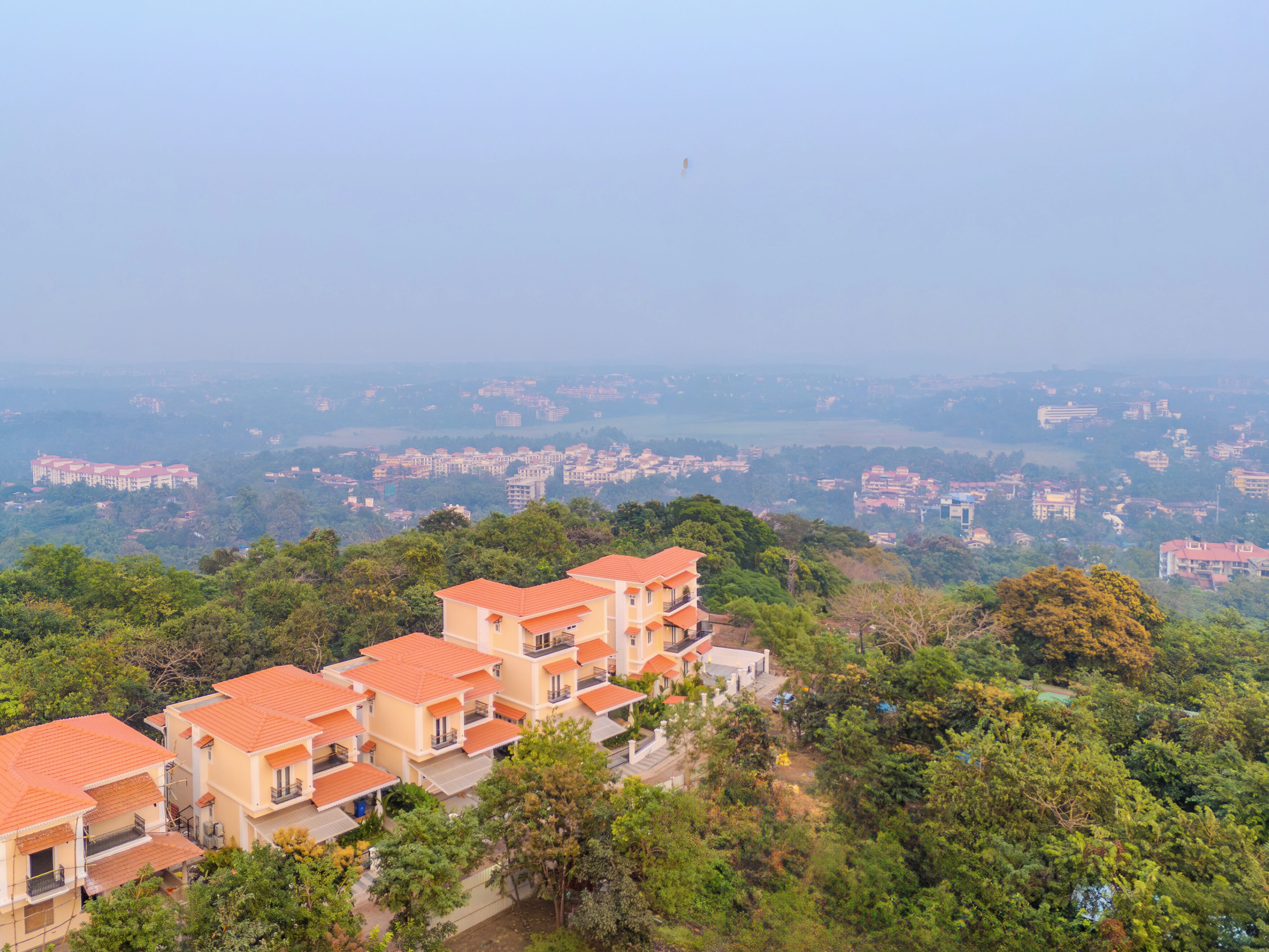 A residential area with multi-story buildings featuring red-tiled roofs and balconies, surrounded by lush greenery.