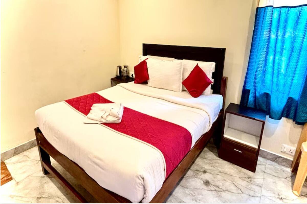 Uma cama bem arrumada com edredom branco e vermelho, cabeceira de madeira e mesa de cabeceira com gaveta.