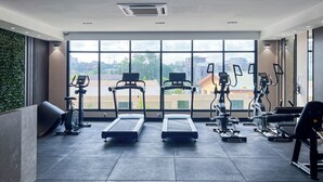 Ett gym med löpband, crosstrainers och motionscyklar, stora fönster med utsikt över staden och en grön vägg.