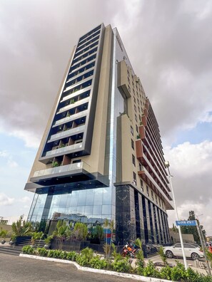 A modern high-rise building with multiple floors, large windows, and balconies with plants. - Snug Studio Haven (Accra)