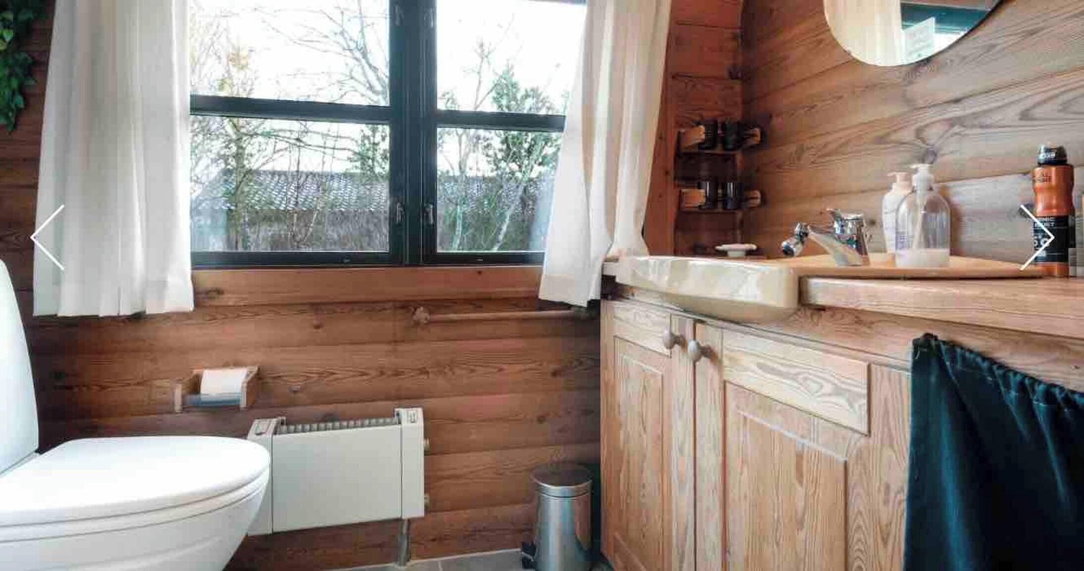 Une salle de bain rustique, aménagée dans une cabane en bois, avec des toilettes, un lavabo et une fenêtre.