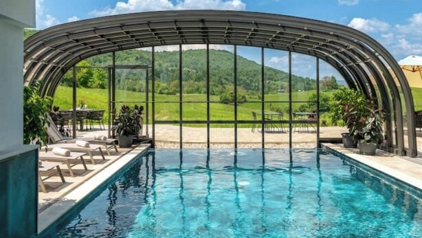 Una piscina con vistas despejadas a un paisaje verde a través de una estructura de cristal curvada.