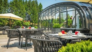 An outdoor patio with round tables and chairs, a glass greenhouse structure, and a backdrop of trees. - Relax in Style: Comfort Room with Private Jacuzzi at Resort Stribor (Severin na Kupi)
