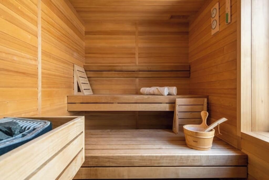 Una sauna de madera con un banco, un cubo de madera y una mesita con una toalla.