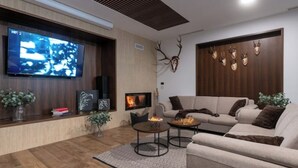 A modern living room with a fireplace, a large flat-screen TV, and mounted deer heads on the wall. - Relax in Style: Comfort Room with Private Jacuzzi at Resort Stribor (Severin na Kupi)