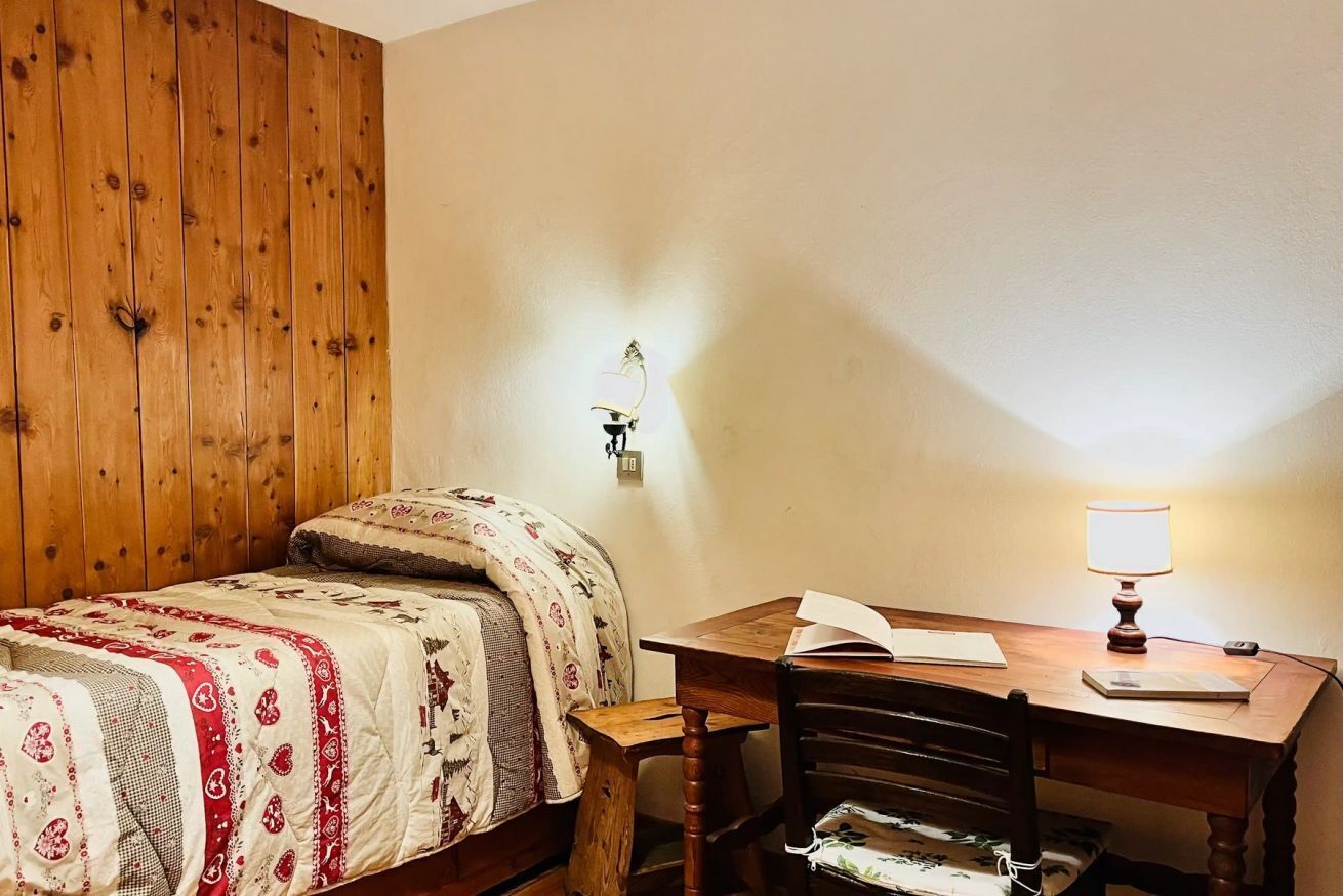 Una habitación con pared de madera, una cama con ropa de cama estampada, un escritorio con una lámpara y una silla.