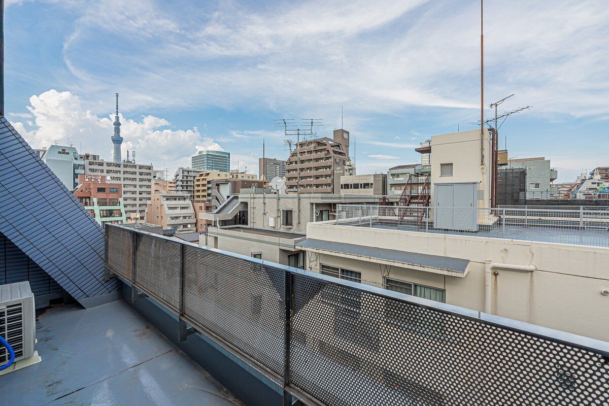 Une vue urbaine avec une tour imposante, divers bâtiments et un toit surmonté d’une clôture métallique.