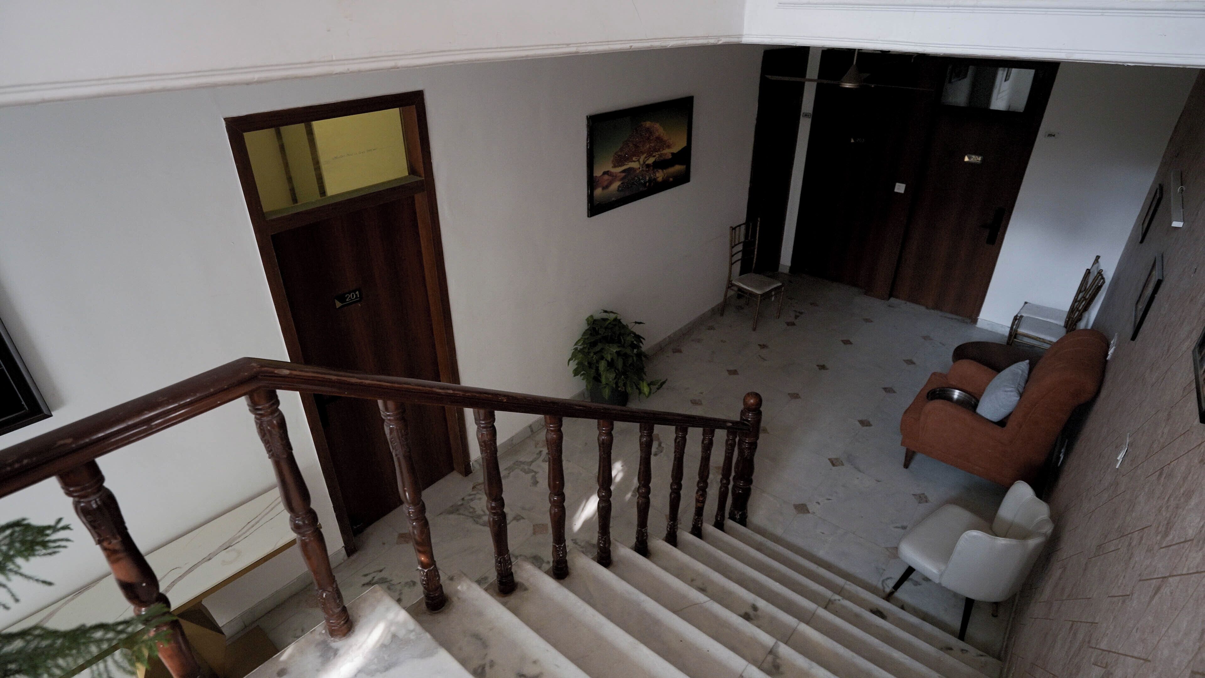 A staircase with wooden balusters, a door labeled '201', a potted plant, and a brown sofa with a white chair.