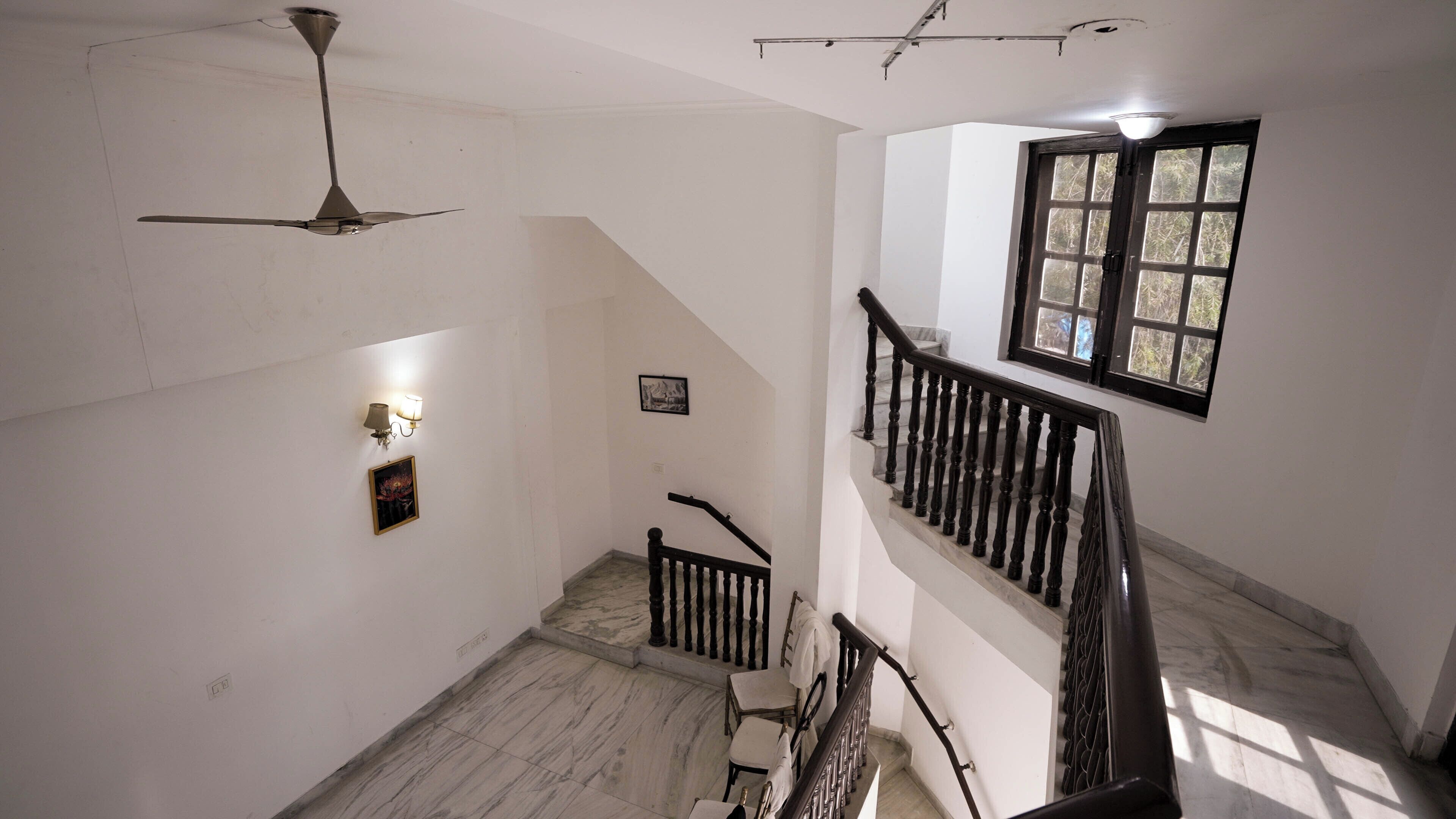 A staircase with a wooden handrail, a ceiling fan, and a window with a view of trees.