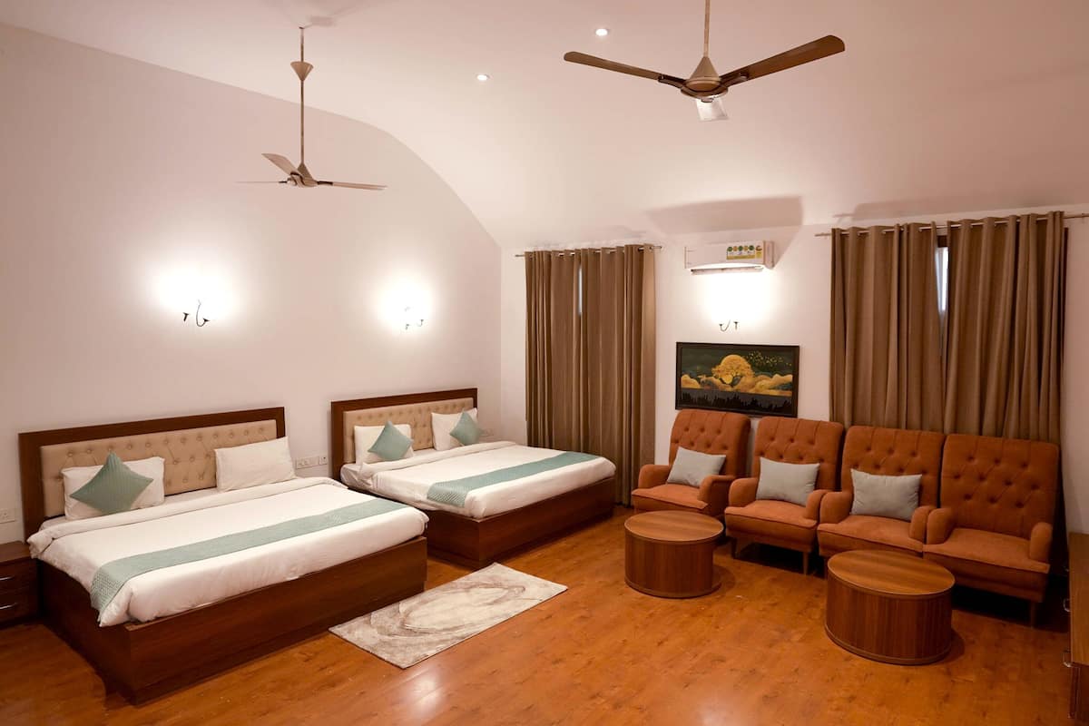 A hotel room with two beds, a sofa set, a ceiling fan, and a painting on the wall.