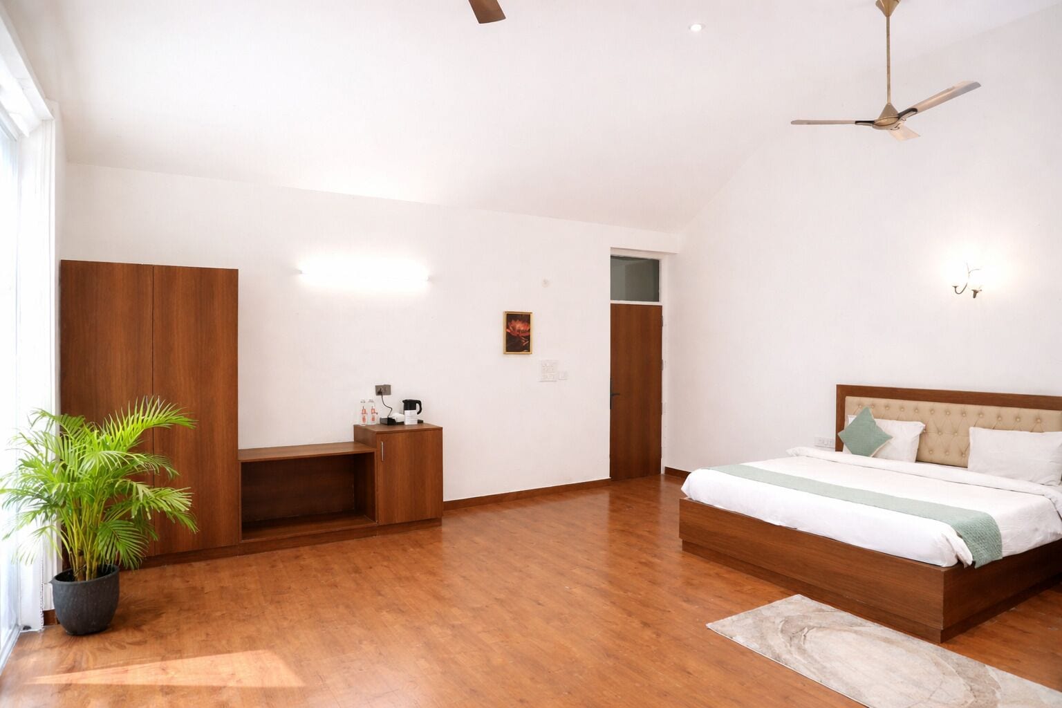 Une chambre à coucher comprenant un lit, un ventilateur de plafond, une table de chevet, une plante en pot et une armoire en bois.