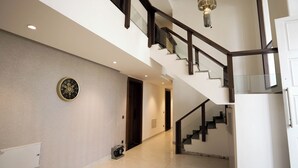 Un intérieur moderne avec un mur orné d’un motif en chevrons, une grande horloge murale, un escalier avec des rampes en verre et un éclairage encastré au plafond.