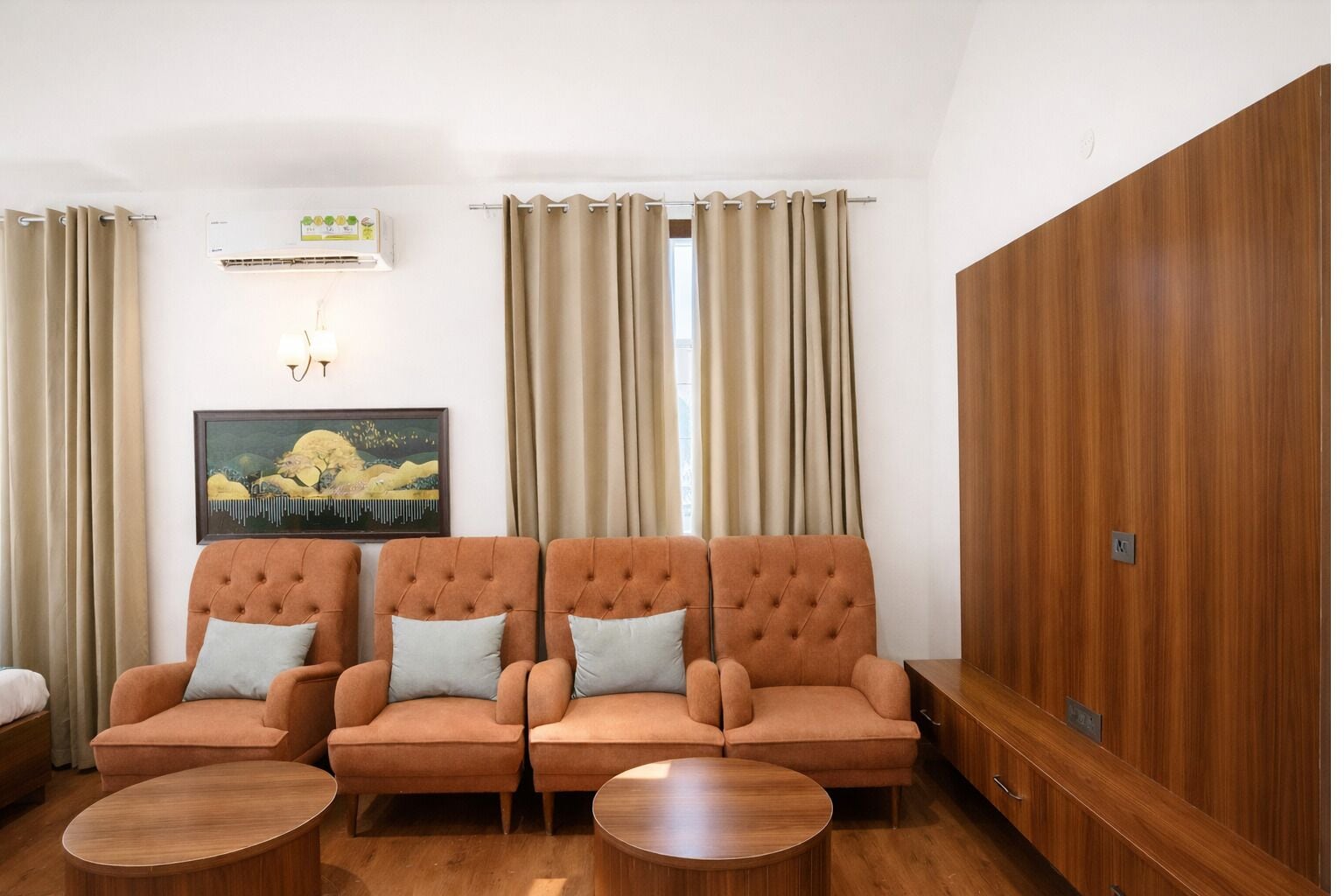A room with three sofas, two round tables, a painting, an air conditioning unit, and a wooden wardrobe.