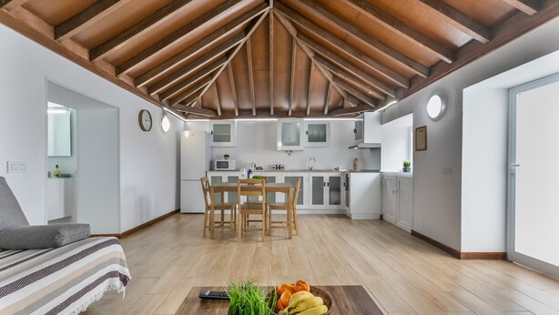 Una cucina moderna con mobili bianchi, una zona pranzo con sedie di legno e un angolo living con divano e tavolino.