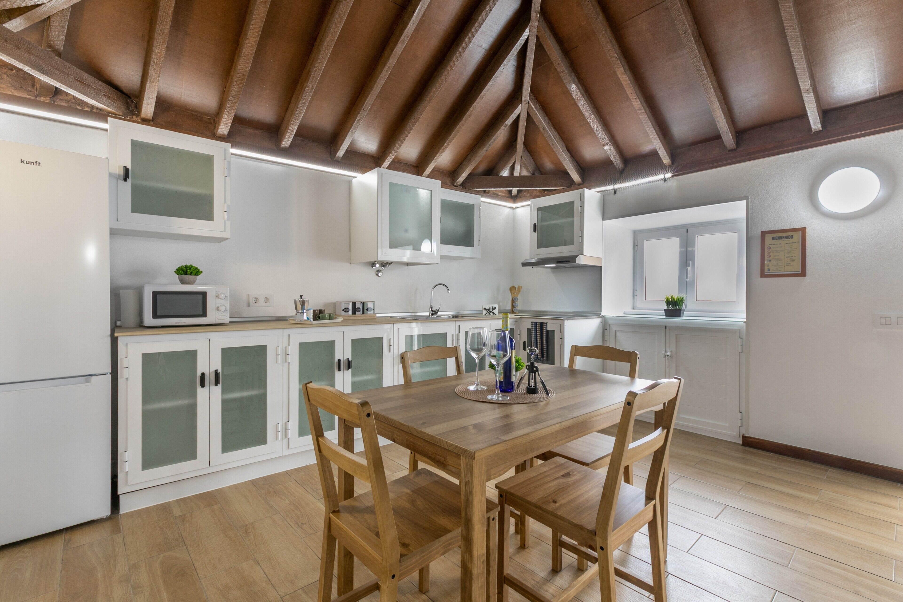 A modern kitchen with white cabinets, a wooden dining table, and a ceiling with exposed beams.