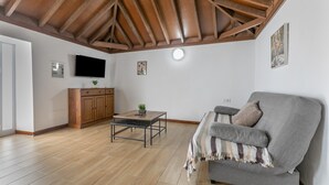Un soggiorno con soffitto in legno, un divano grigio, un tavolino, una TV e mobili contenitori in legno.