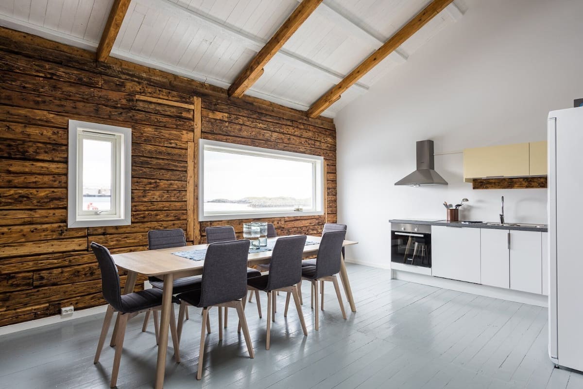 A modern kitchen with wooden beams, a dining area with a table and chairs, and a view of the outdoors.